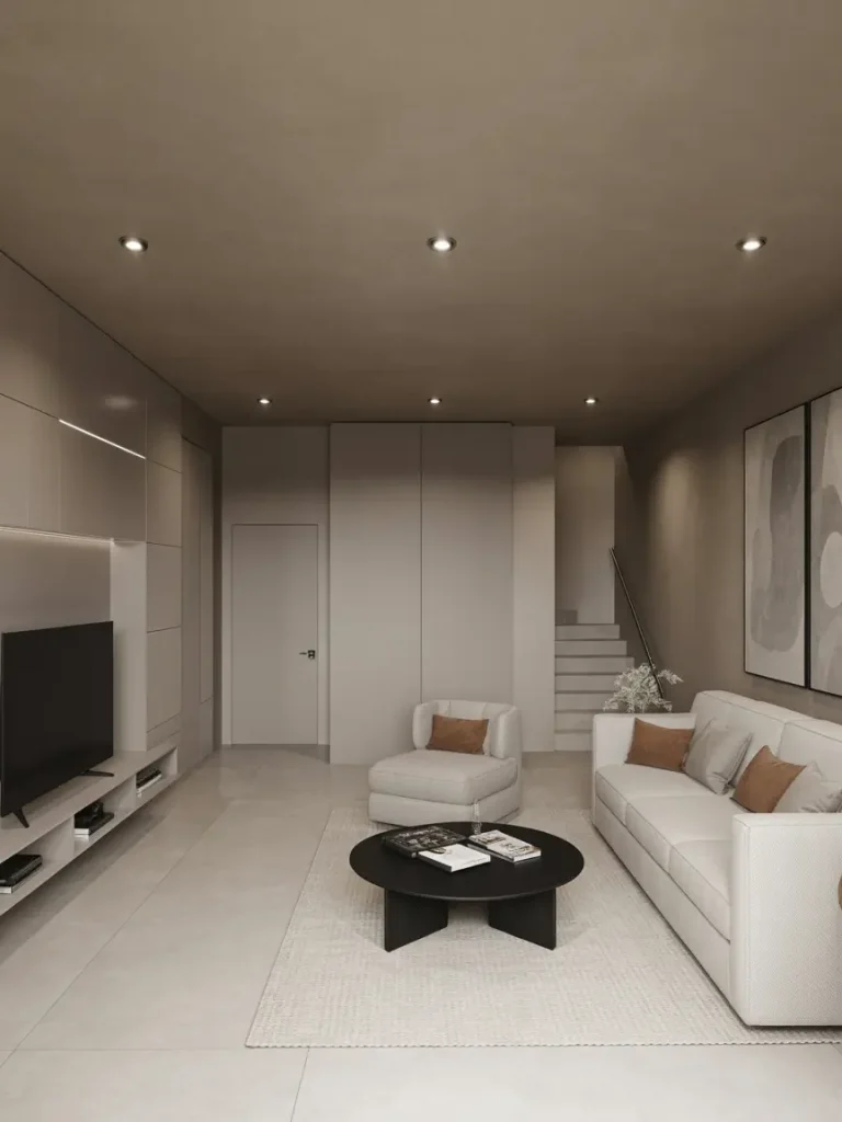 Modern basement living room with minimalist décor, white sofa, accent pillows, black round coffee table, and built-in TV wall unit.