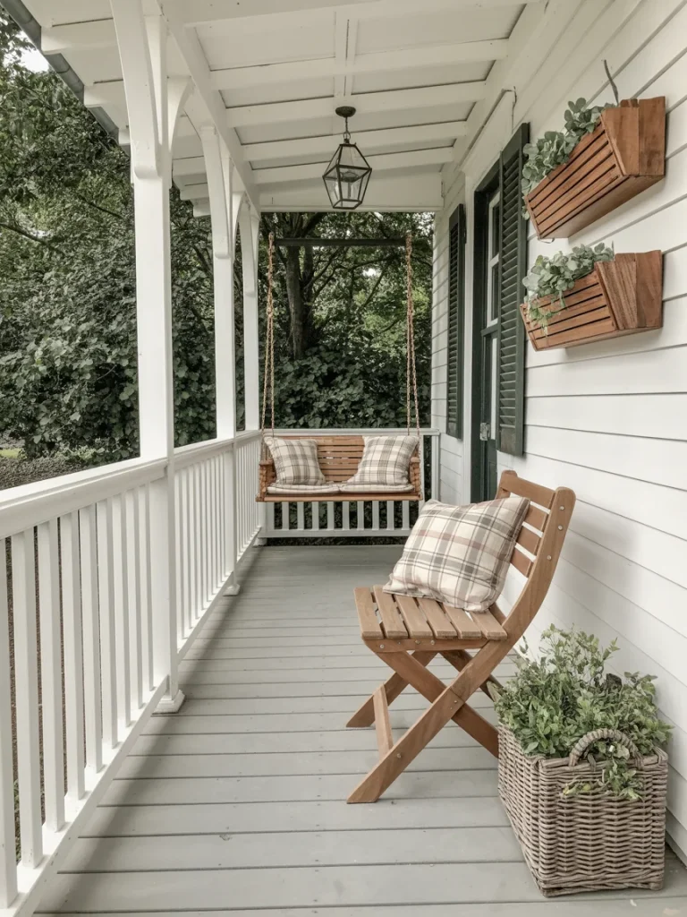 Small farmhouse porch with a wooden swing, plaid pillows, potted greenery, and wall-mounted wooden planters.