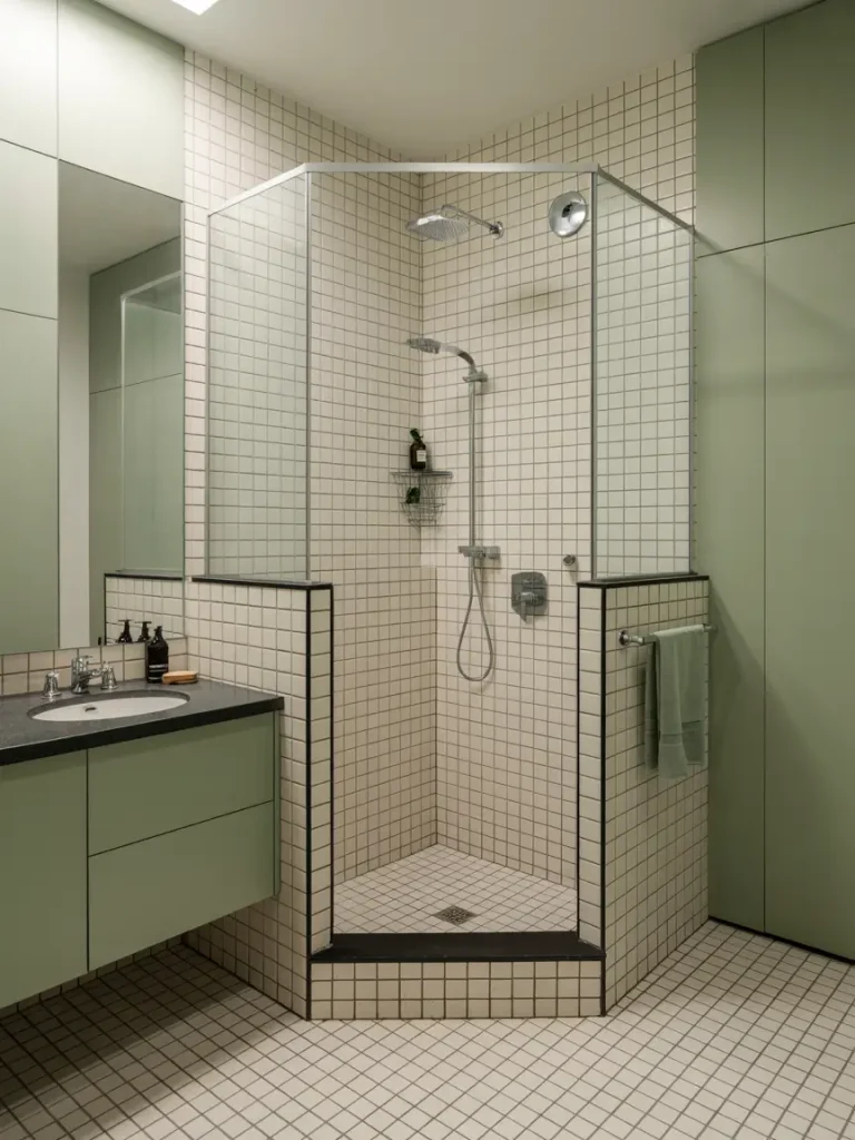 Small modern shower with tiled walls and floor, glass enclosure, and black fixtures in a minimalist bathroom.